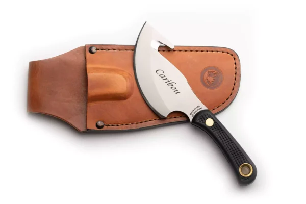 Knives of Alaska Caribou knife with black Suregrip handle and gut hook blade resting on leather sheath